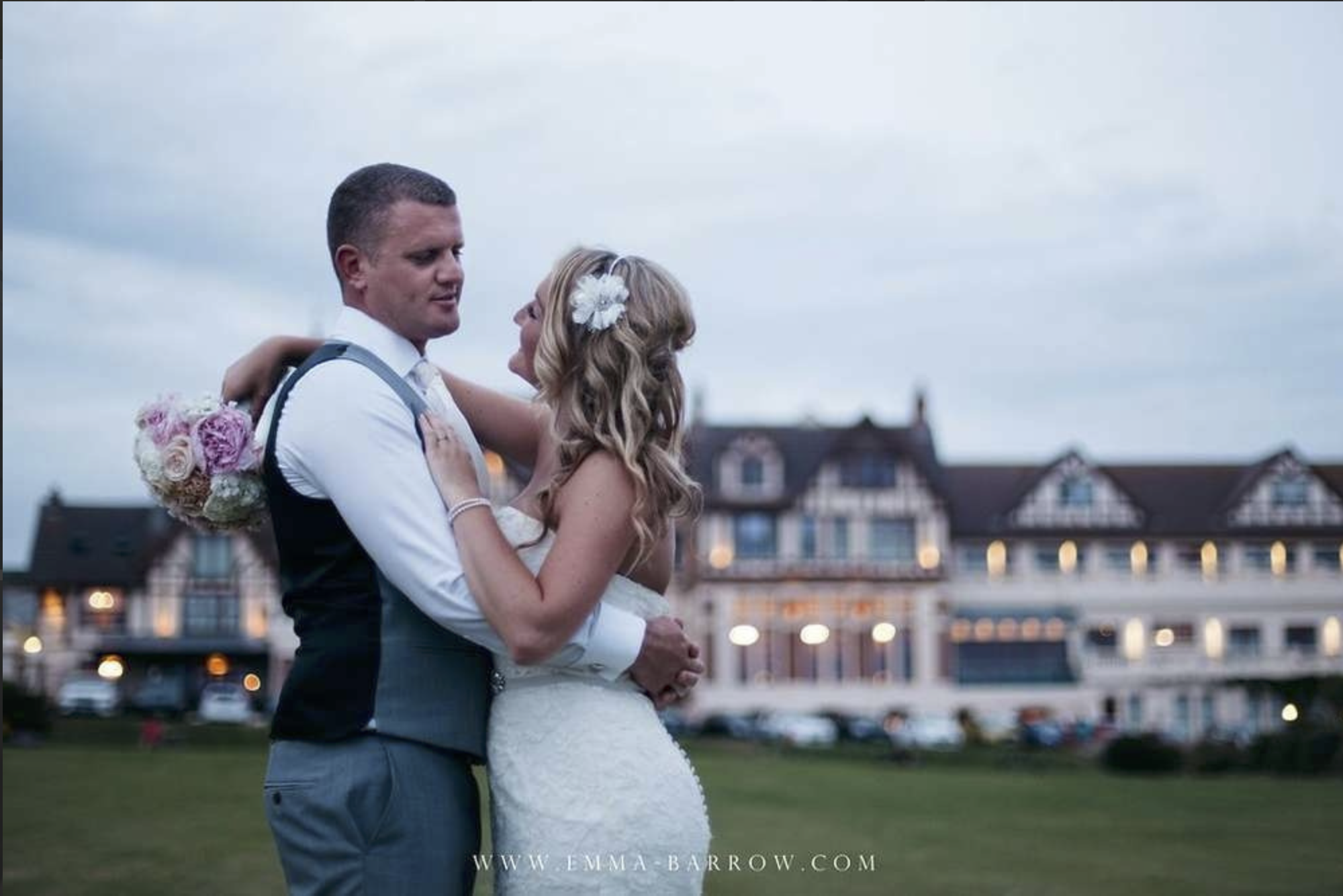 A bride and groom in the grounds with the hotel behind them