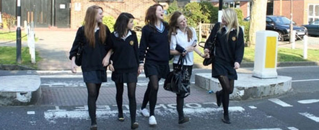 five young people laughing crossing the road