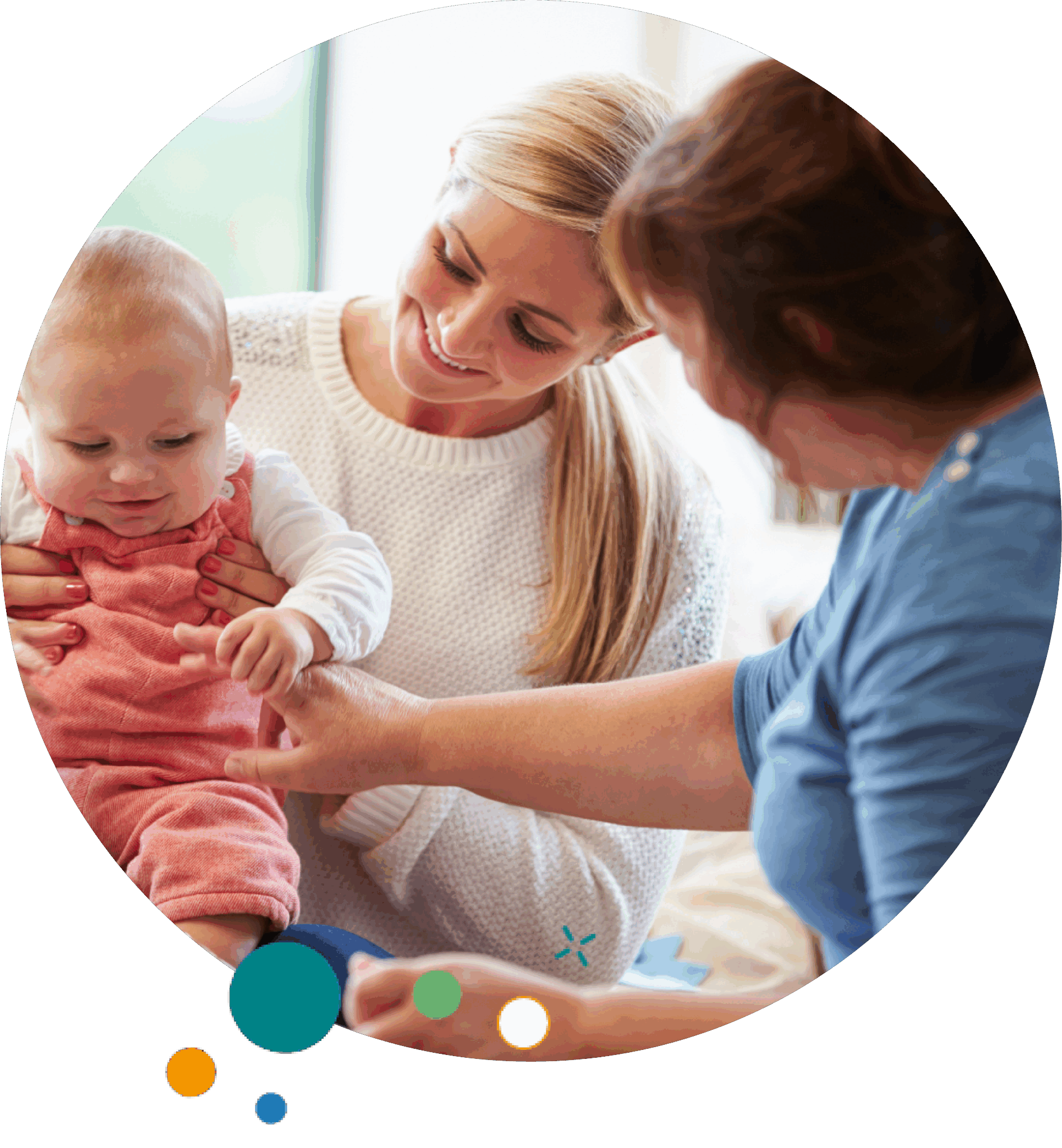 A smiling woman holds a baby dressed in pink overalls while another woman interacts with the baby. The scene conveys warmth, care, and community support.