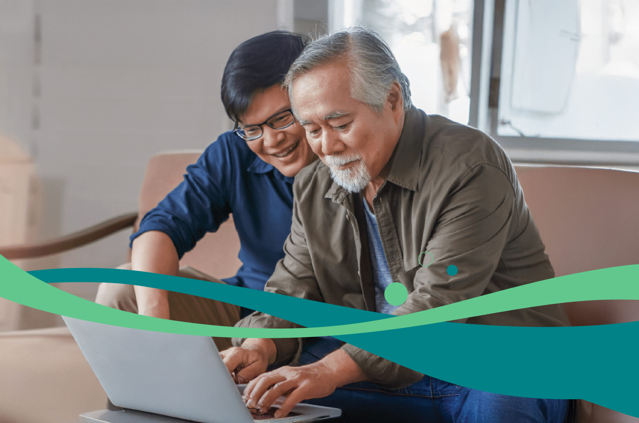 Two people sitting indoors, focused on a laptop placed on a table in front of them. A teal and green wave graphic runs across the bottom of the image.