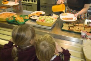 2 children seen from the back being served school dinners