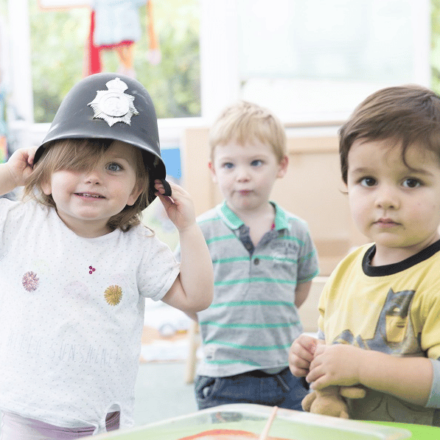 a group of 3 young children one is wearing a toy police helmet
