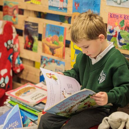 a young boy in school uniform reading a book in a library corner