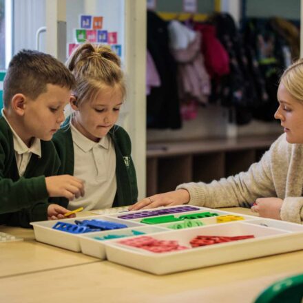 a teacher with two young children with a tray of small coloured discs