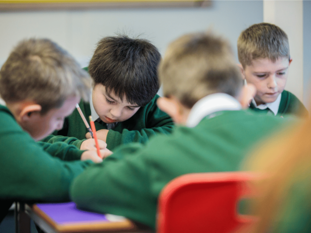 Four young boys in green sweatshirts concentrating and writing