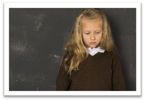 School girl standing infront of a blackboard looking sad.