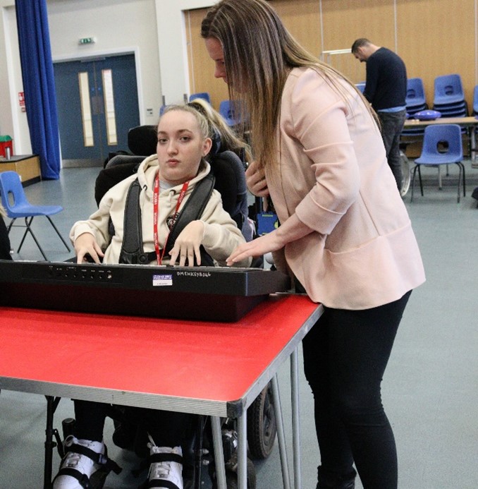 Girl in wheelchair playing a keyboard placed on a red table