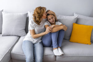 Woman talking with unhappy looking teenage girl on sofa