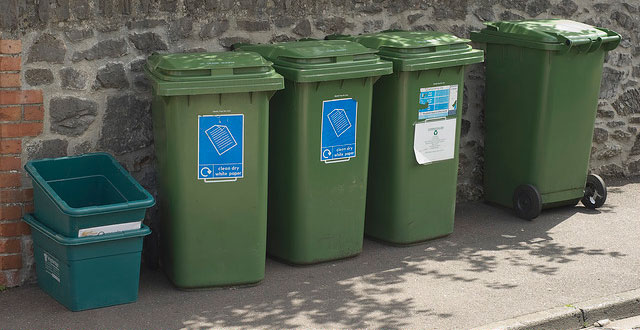 Some green recycling bins lined up in front of a wall