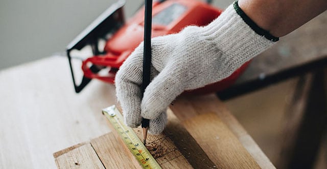 A close-up of a tradesman's hand measuring some wood with a measuring tape and a pencil