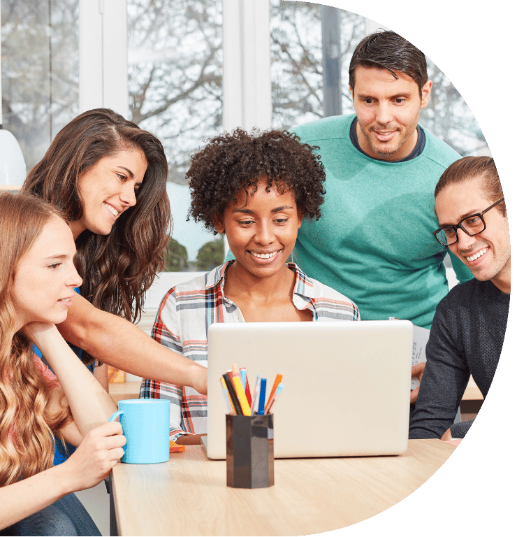 Picture of a group of five adults, Three are sitting around a laptop, the other two are standing behind them working as a team.