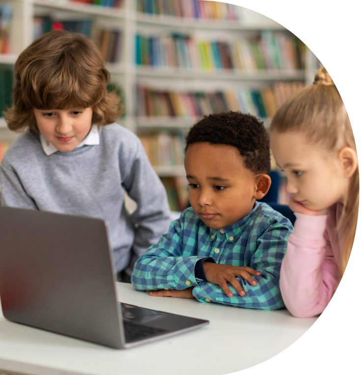 three young children sat in a classroom looking at a laptop