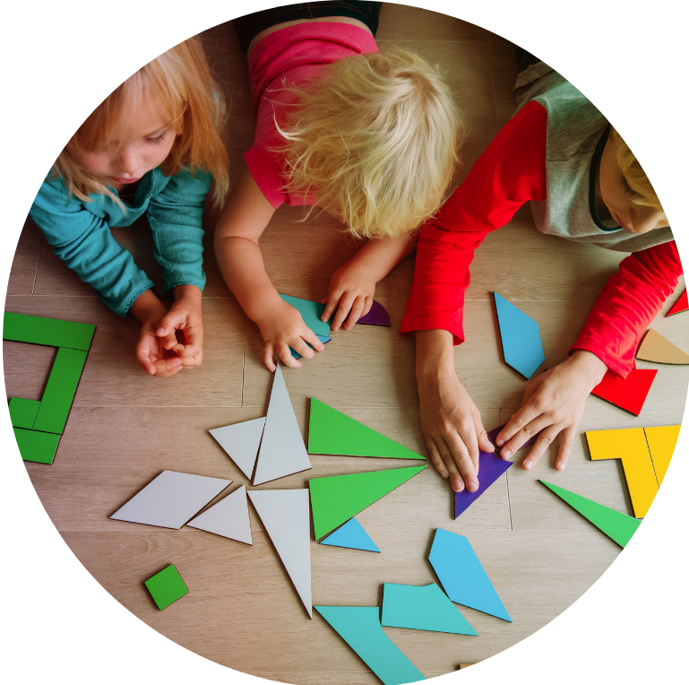 Picture taken from above of three children lying on the floor doing arts and crafts with paper cutouts in front of them.