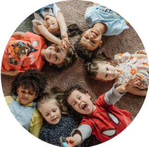 children lying down on their backs on a carpet in a circle looking up at the camera