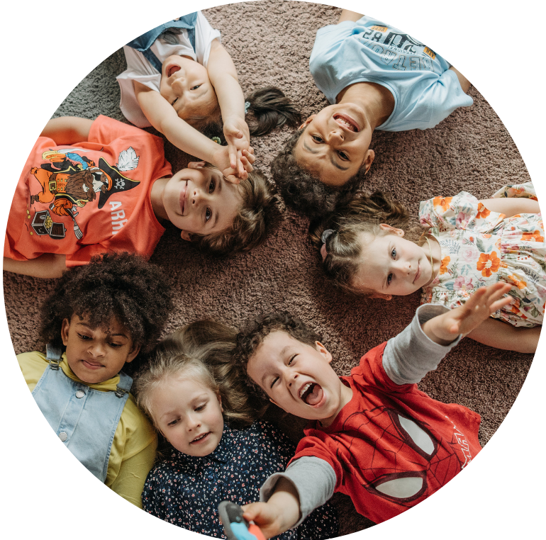 children lying down on their backs on a carpet in a circle looking up at the camera