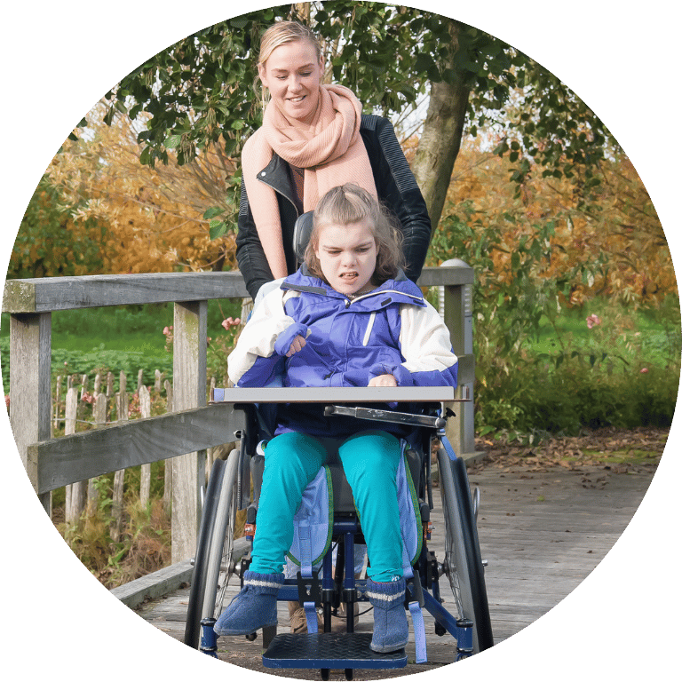 Image shows an adult pushing a disabled child in a pushchair on an autumn day