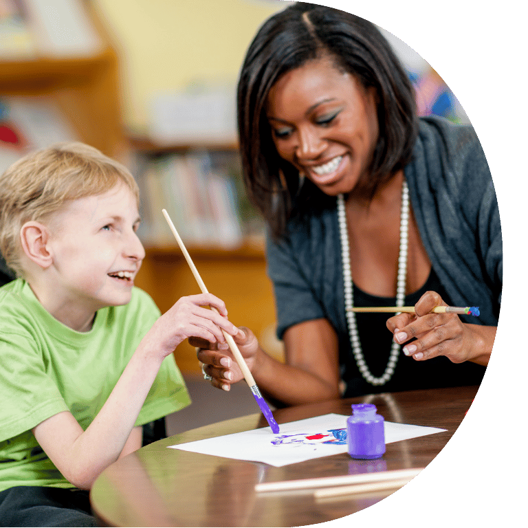 Image is cropped to a D shape and shows a disabled child painting with an adult.