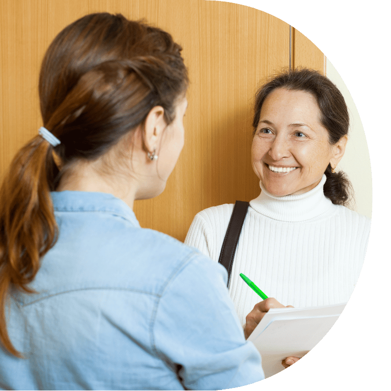 The image is cropped to a D shape and shows two women looking at each other. One has their back to the camera and the other is smiling.