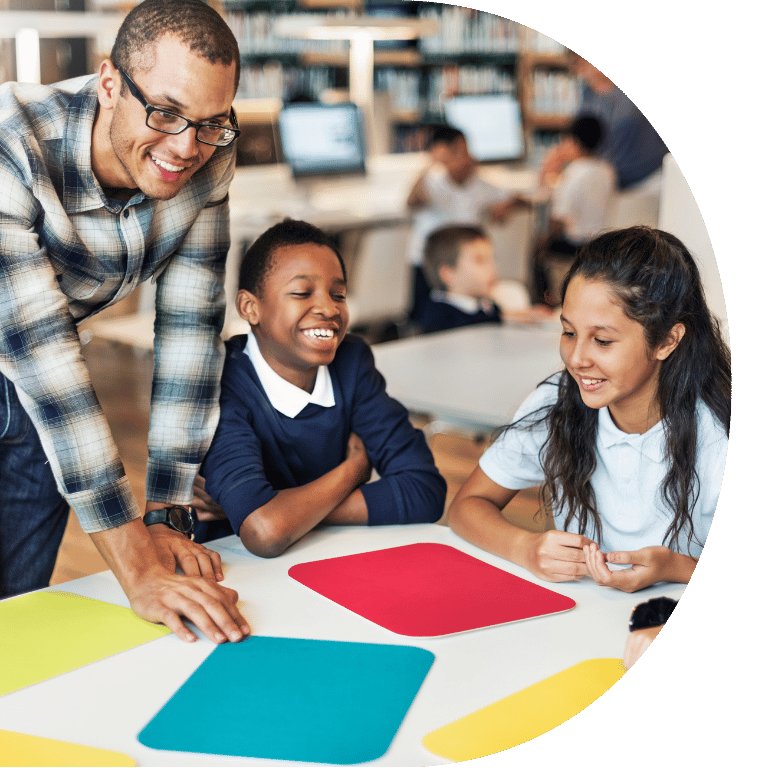 The image is cropped in a D shape and shows a teacher leaning over a table of students.