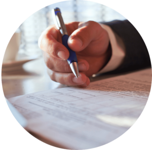 Picture of a hand holding a pen, signing a document.