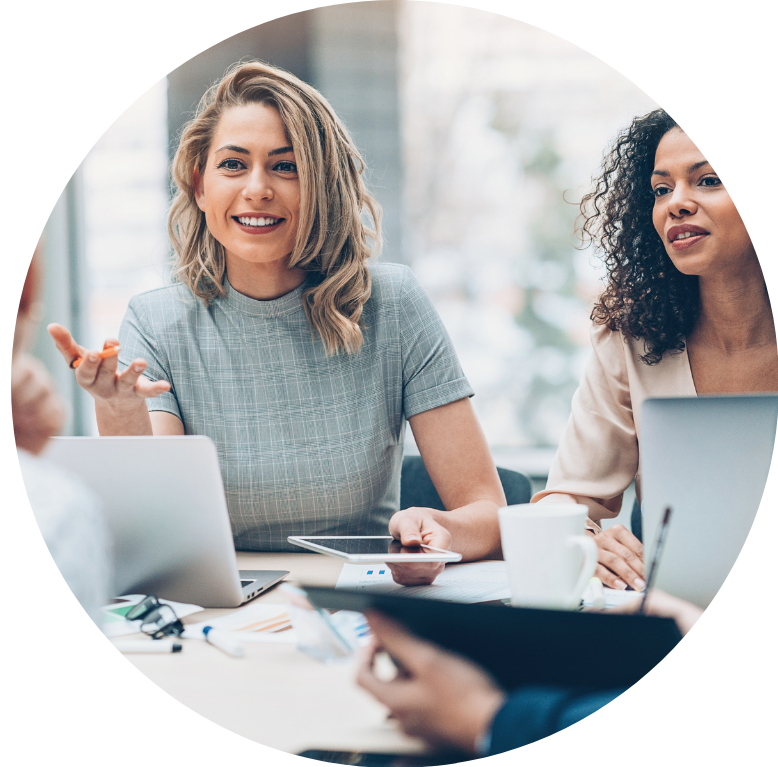 Picture of a three people in a meeting. One of them is off camera. The other two are facing them discussing work. All have laptops in front of them.
