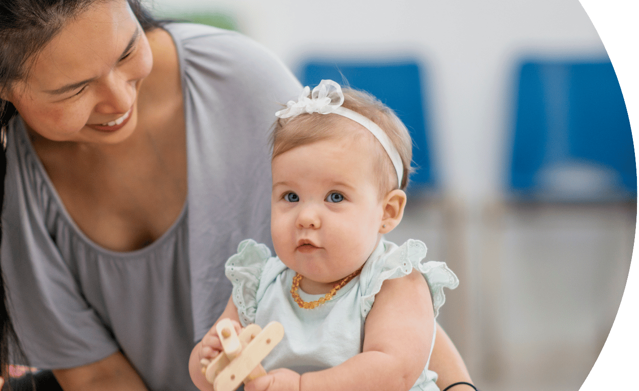The image shows a baby looking at the camera and playing with toys and an adult sat with the child. The image is curved on the left hand side.
