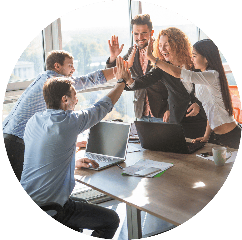 Picture of five people in a meeting environment. They are happily doing a high five across the table.
