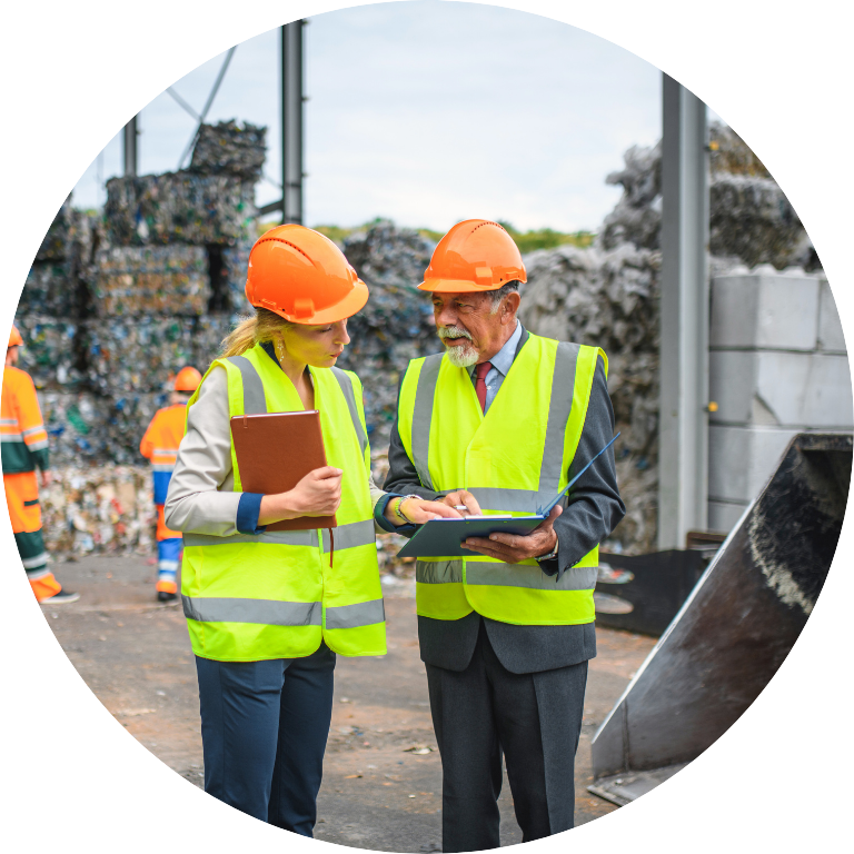 The image is cropped in a circle and shows two people in high-vis vests and hard hats in front of recycling centre.