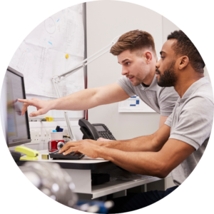 The image is cropped in a circle and shows two people gathered round a computer working together,