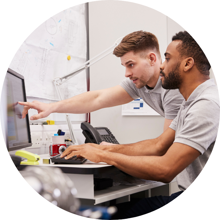 The image is cropped in a circle and shows two people gathered round a computer working together,