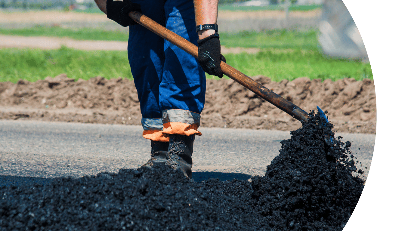 Image shows a close up of someone shovelling tarmac
