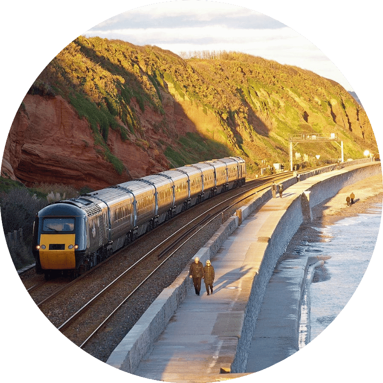 Image shows a train travelling along a coastline on a sunny day.