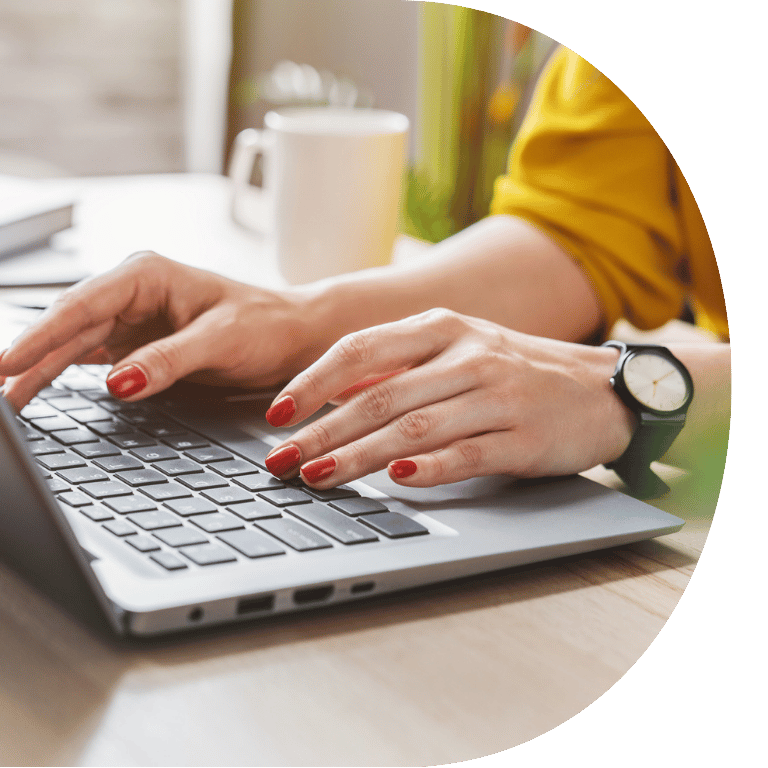 The image is cropped in a D shape and shows a close up of hands typing on a laptop.