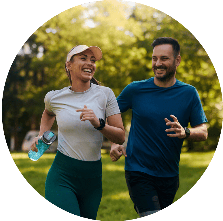 Two people jogging through a park together smiling.
