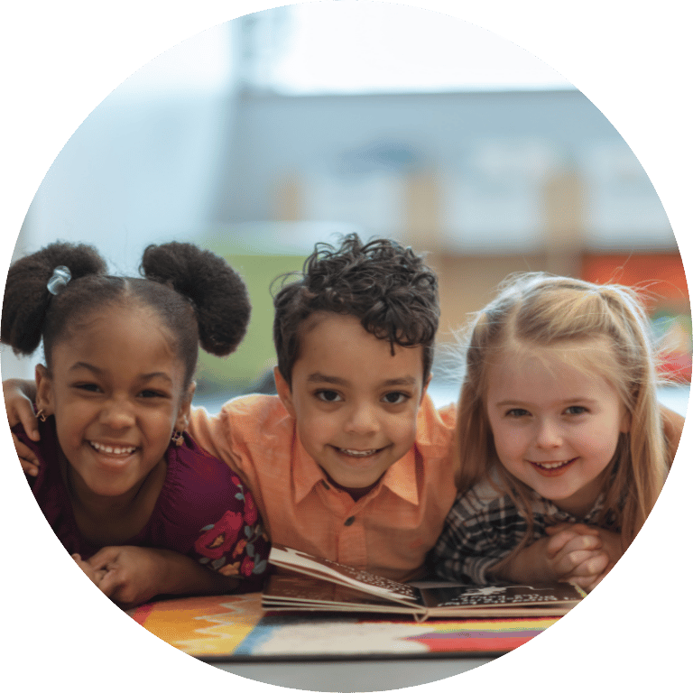 The image is cropped in a circle and shows three children smiling and reading a book