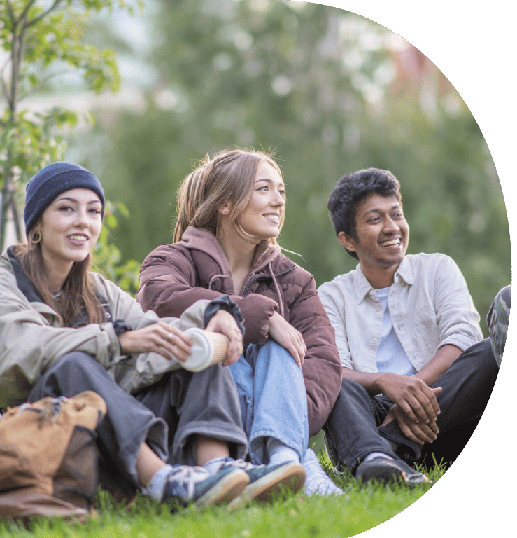 Picture of three young adults sitting on the grass in a park, smiling.
