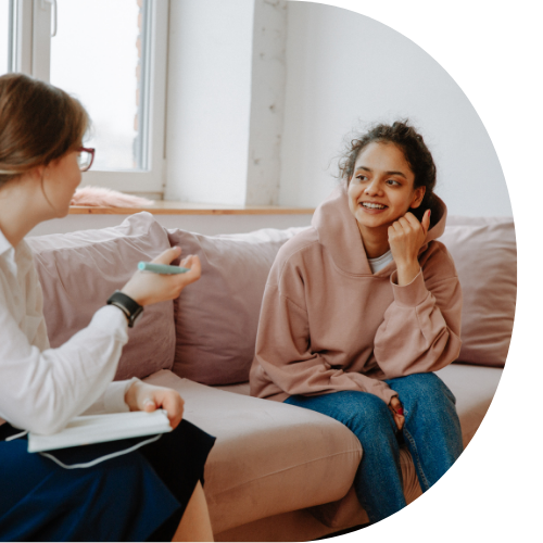 Image shows a young adult on a sofa smiling at an adult.