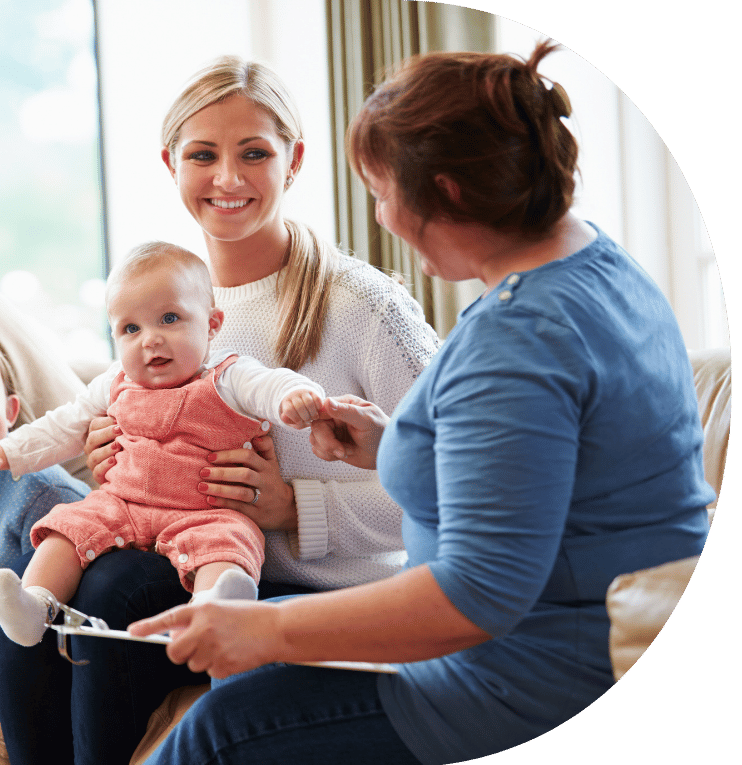 A family with a small child talk to somebody sat on a sofa.