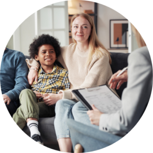 Image shows a smiling family sat on a sofa, with a support worker opposite with a clipboard