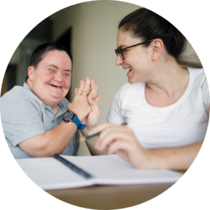 Image shows a young adult with disabilities high fiving the adult next to them at the table