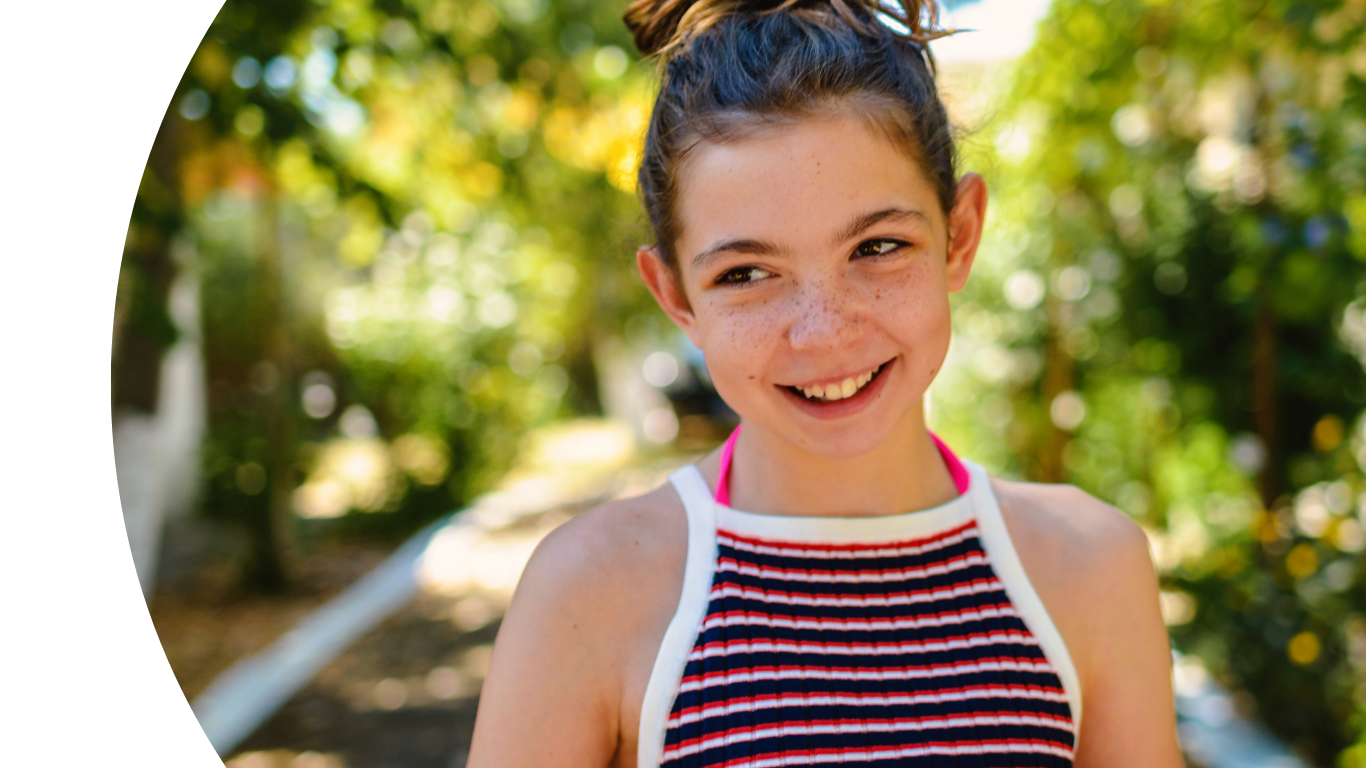 a young teen smiling to the left of the camera, standing in woodland