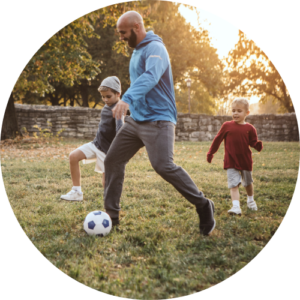 An adult and two children playing football on grass