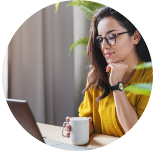 Adult sitting at desk working on laptop, drinking coffee.