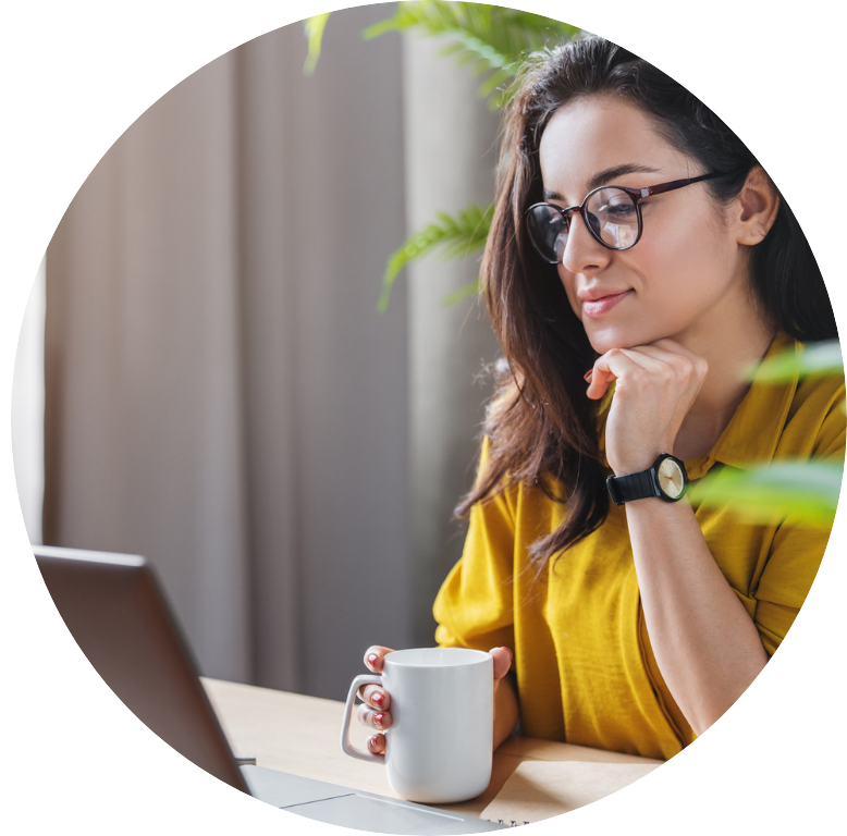 Adult sitting at desk working on laptop, drinking coffee.