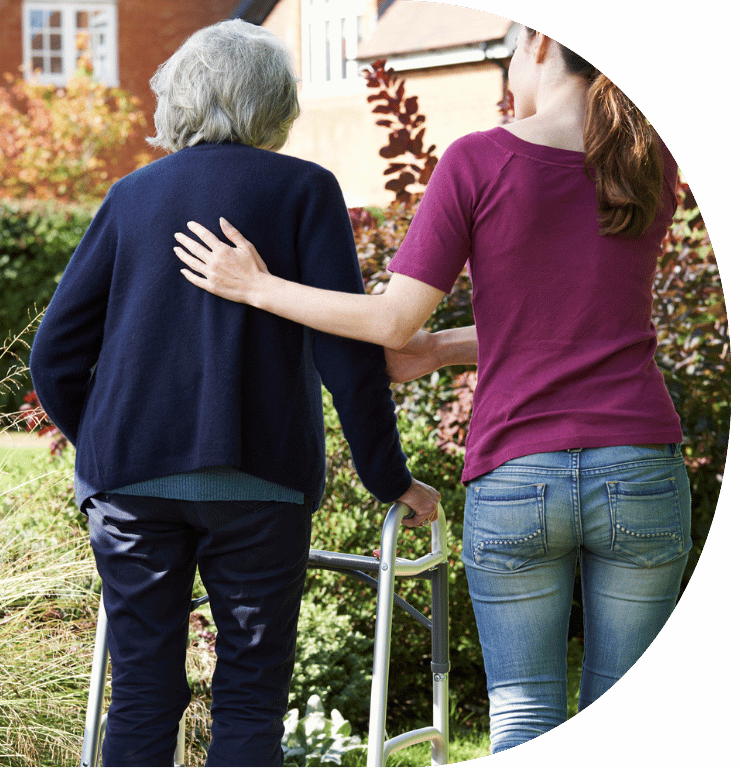 Picture of a adult helping an elderly adult using a walker. Picture taken from the back.
