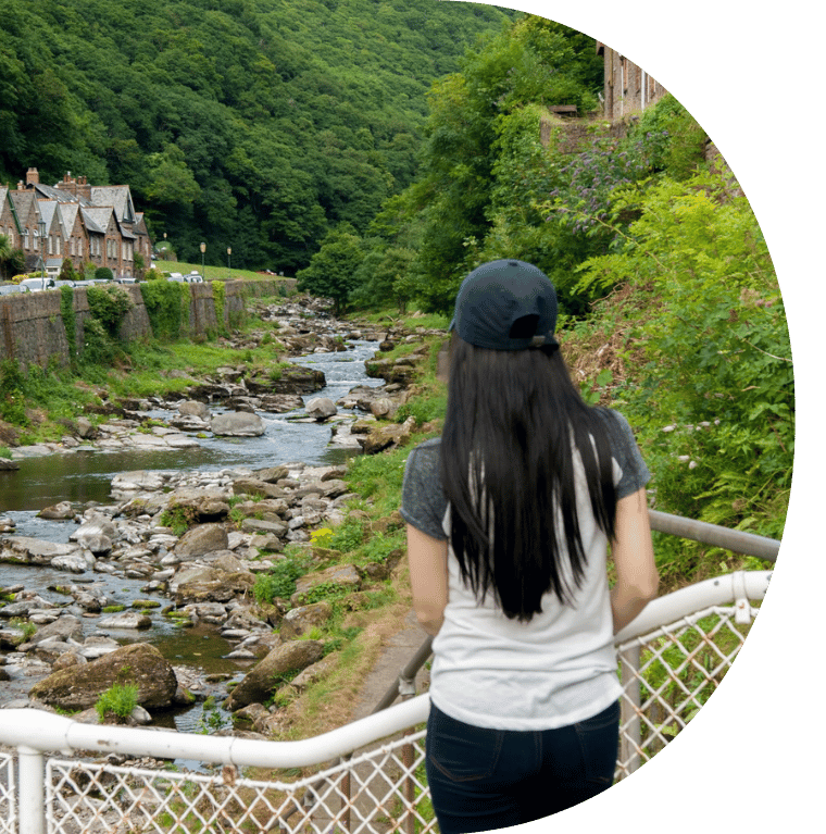 A person looking out over a small river, surrounded by trees and greenery