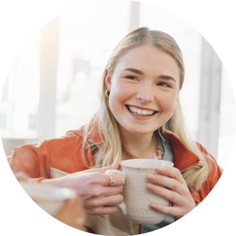 A person smiling looking just off camera, with both hand holding a mug.