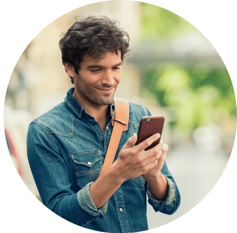A person outside smiling at their phone in their hands.