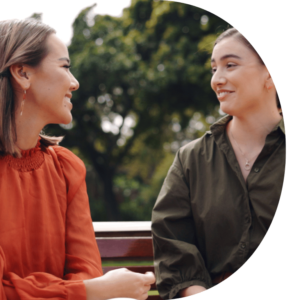 A close up of two people sat on a park bench smiling at each other.