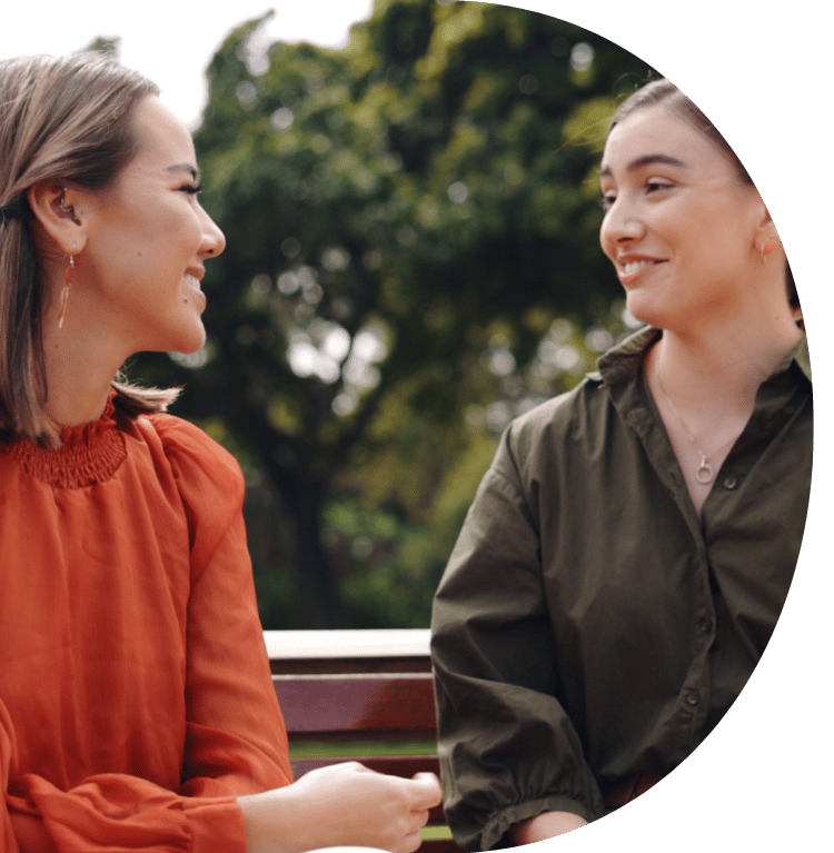 A close up of two people sat on a park bench smiling at each other.